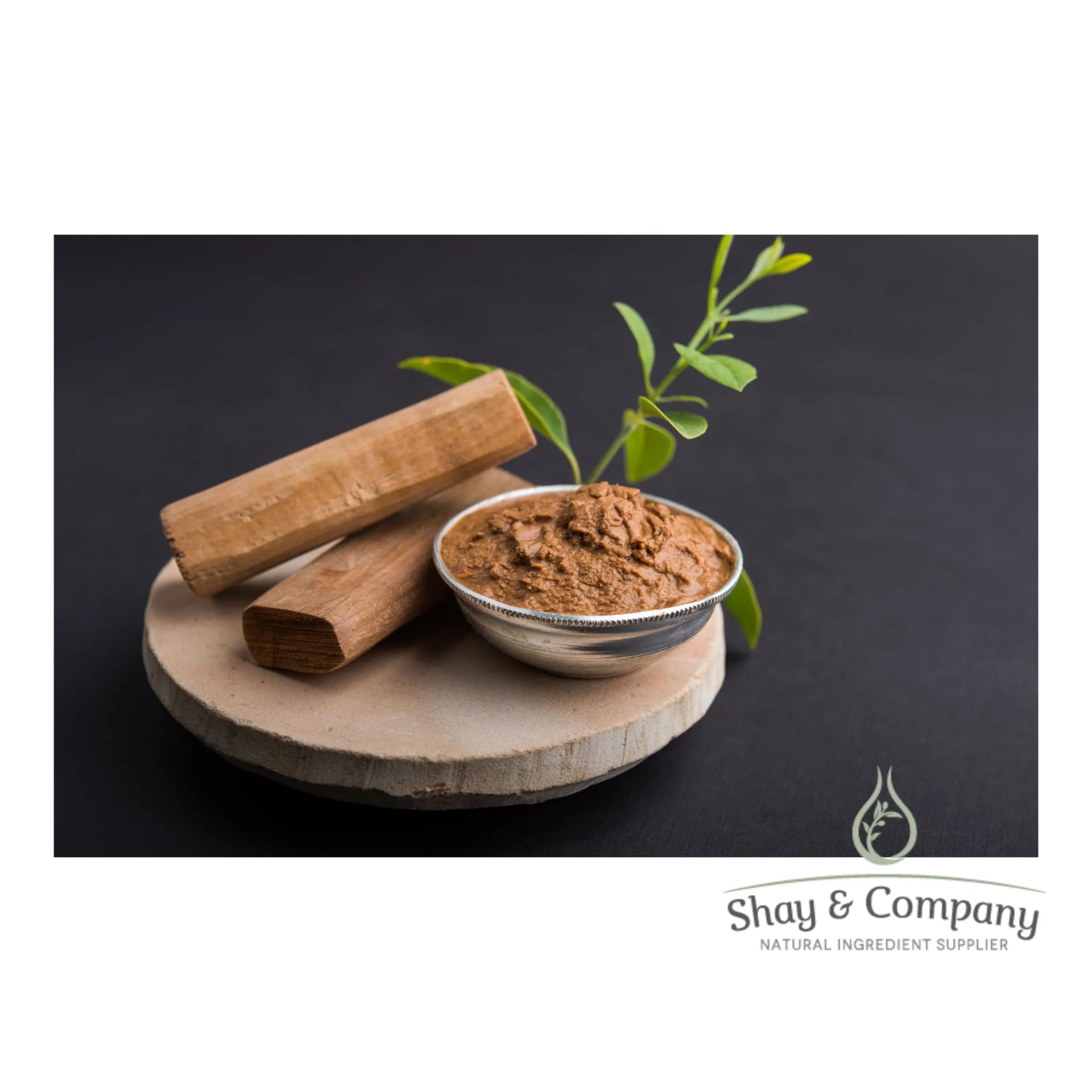 Two pieces of sandalwood and a metal bowl of ground sandalwood sit on a round wood base on a black background