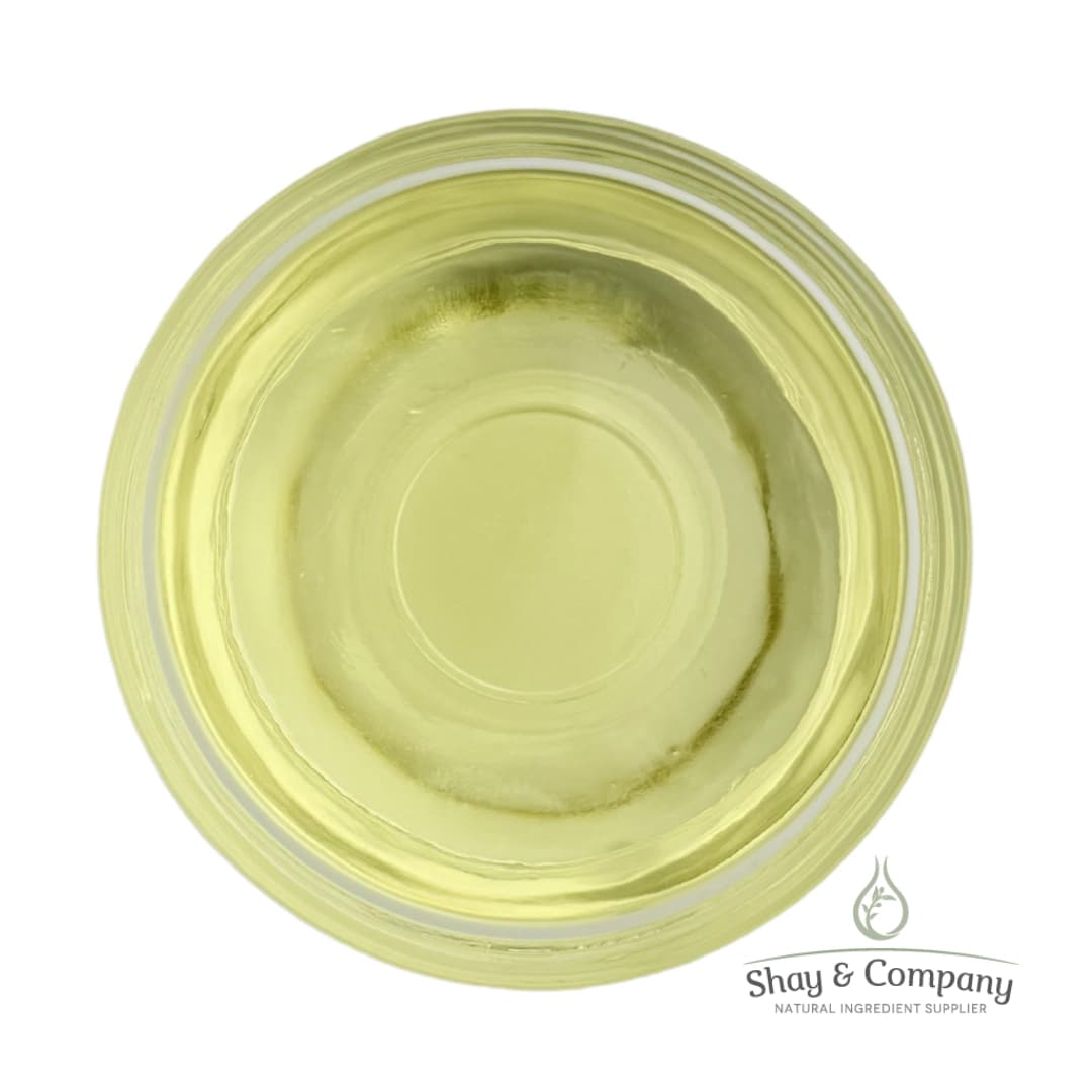 Top-down view of pale yellow natural oil in a clear glass dish with Shay & Company logo.