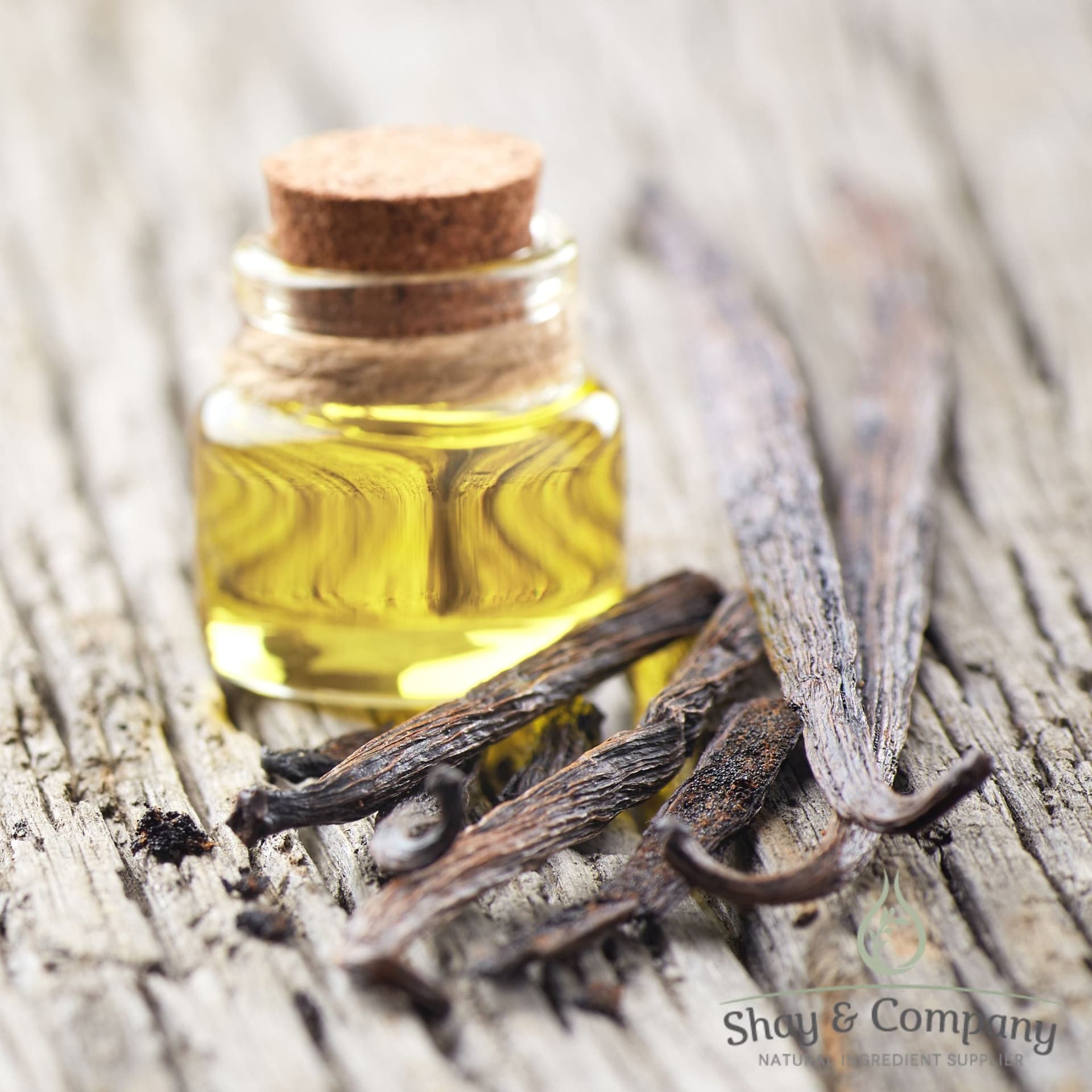 Vanilla bean extract in glass bottle with cork next to whole vanilla pods on weathered wood surface.