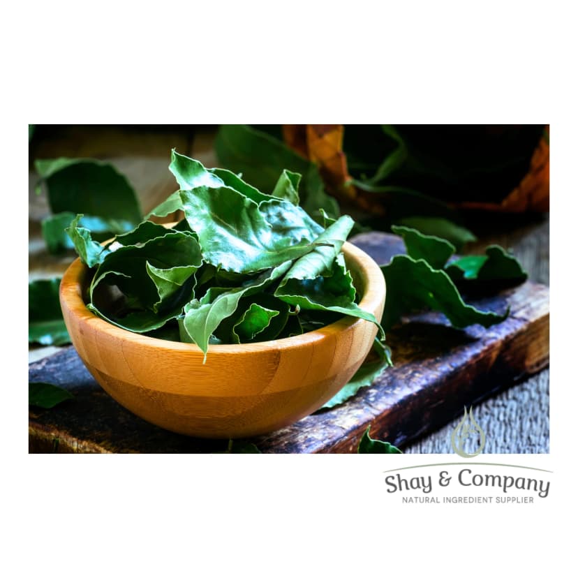 A wooden bowl sits on a wooden cutting board. Bowl is filled with bay leaves that spill onto the cutting board