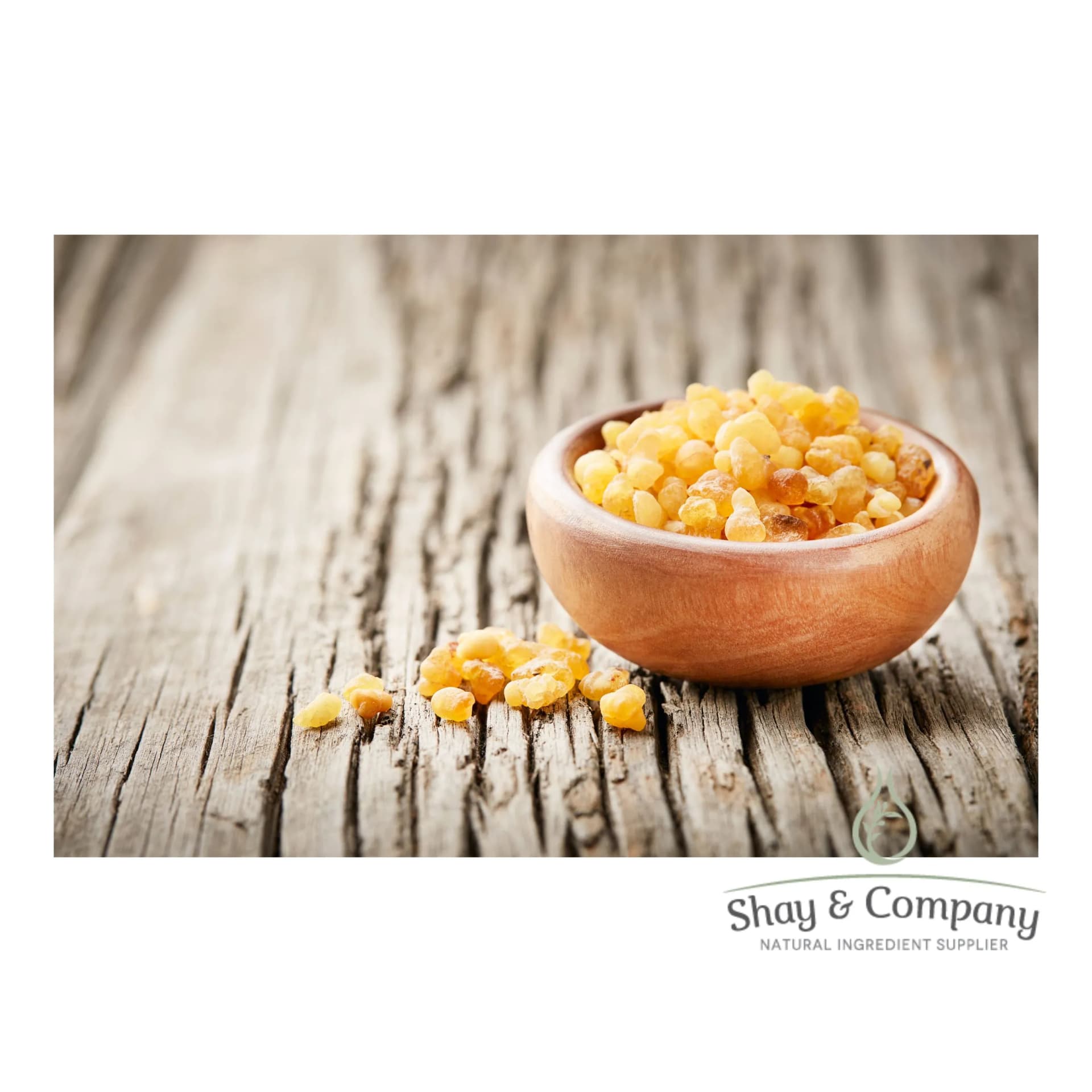 A wooden bowl sits on a wooden table. The bowl has Frankincense nuggets filling it and spilling onto the table.