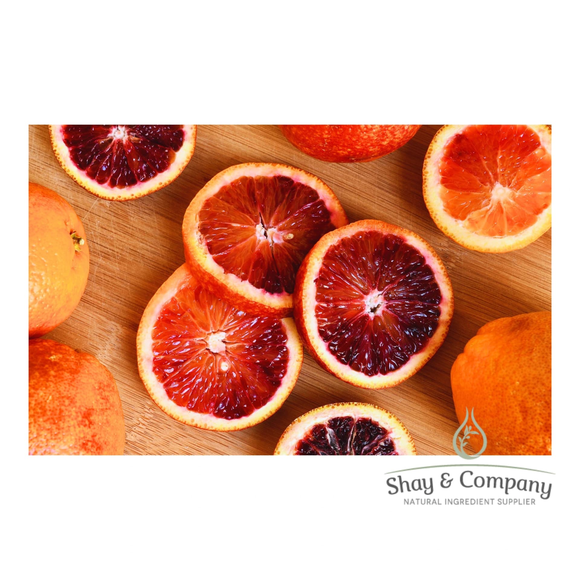 A variety of cut blood oranges on a wooden counter. Three full oranges are around the edge.