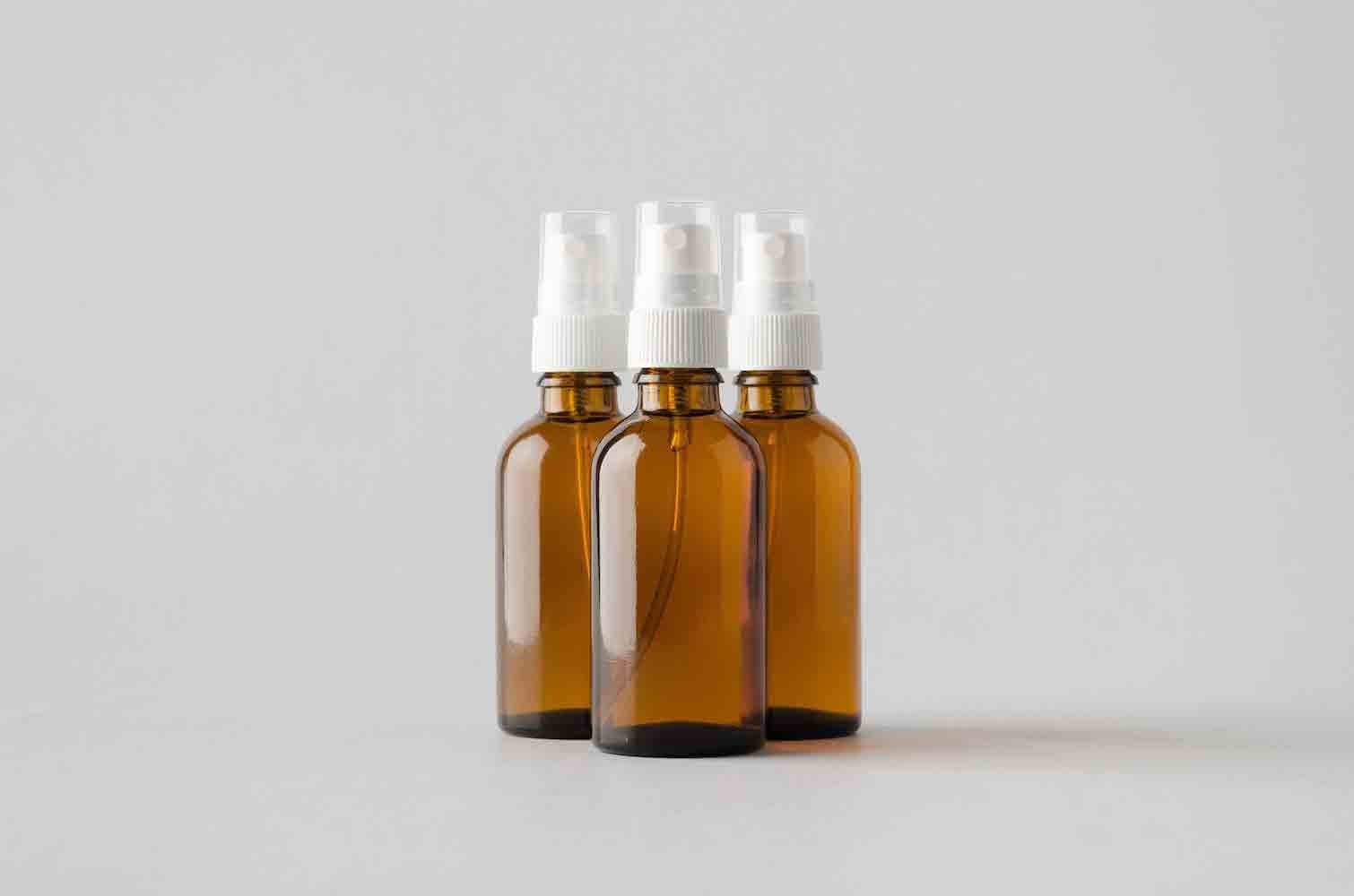 Three amber glass spray bottles with white mist dispensers on a light gray background.